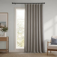 Gray curtain hanging in a room with a window, side table, and chair.