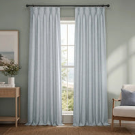Light blue curtains hanging in a room with a window, chair, and side table.