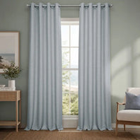 Light gray curtains hanging in a room with a window, side table, and chair.