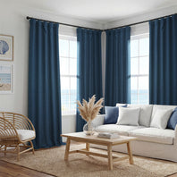 A set of deep navy blue grommet curtains hanging on a black rod in a bright, modern living room with a white sofa, wooden coffee table, and ocean view windows.