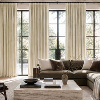 Living room with a brown sectional sofa, marble coffee table, and large windows with white curtains.