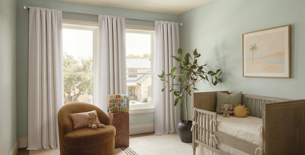 Soft white linen curtains add an airy, calming touch to this peaceful nursery. Their lightweight texture gently filters natural light while complementing the soft sage walls, warm wood crib, and neutral décor, creating a bright, cozy space perfect for rest and play.