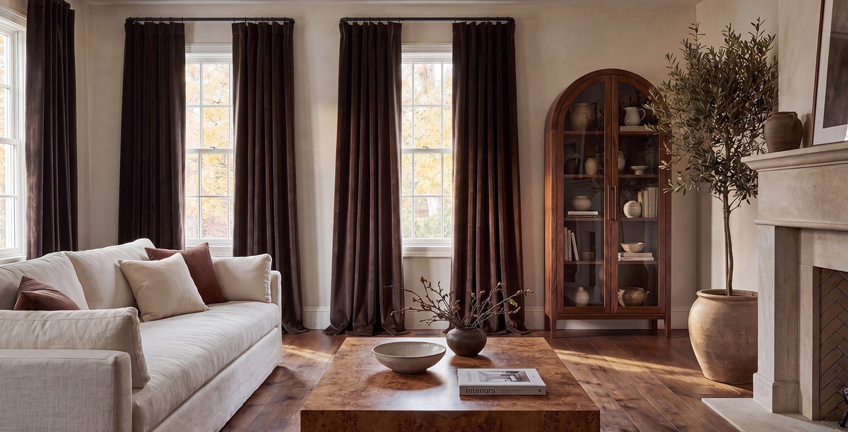 Mauve velvet curtains frame tall arched windows in an elegant bedroom with soft neutral furnishings and blush accents.