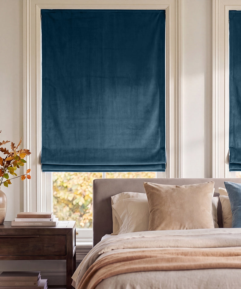 Avalon Blue: Deep navy velvet Roman shades frame bedroom windows, complementing crisp white bedding and warm autumn accents.