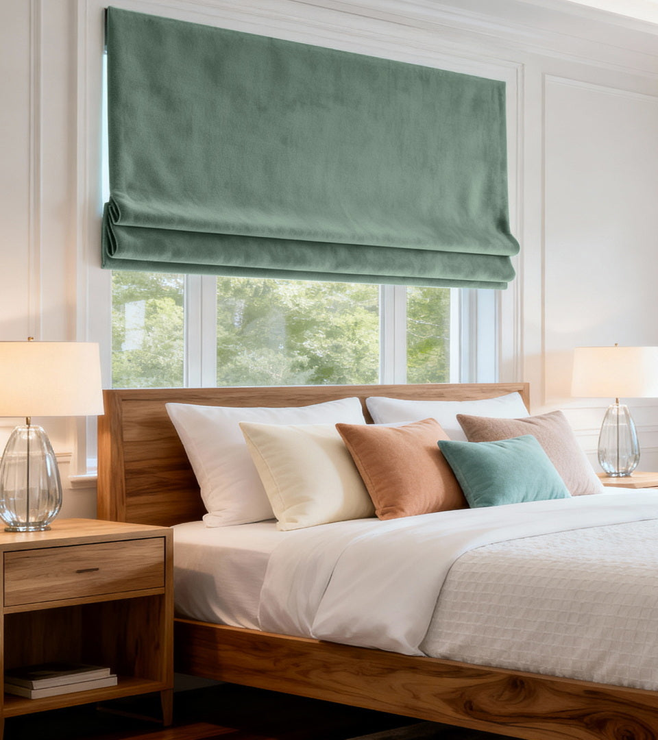 Aqua Mist Roman shade covering a bedroom window above a wood bed with white bedding and bedside lamps.