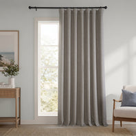 Gray curtain hanging in a room with a window, side table, and chair.