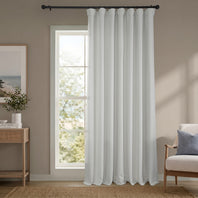 White curtain hanging in a room with a window, side table, and chair.
