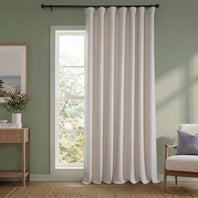 White curtain hanging in a room with a green wall, a small table with decor items, and a chair.