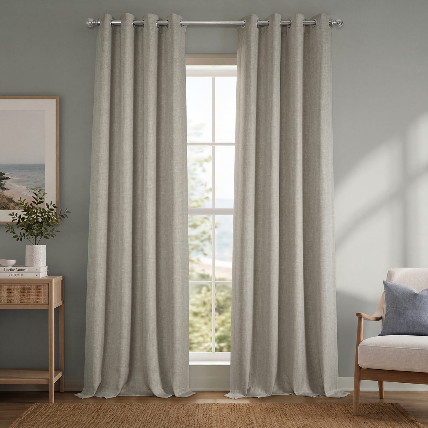 Pair of beige curtains hanging in a window with a view of greenery, a chair, and a side table with decor items.