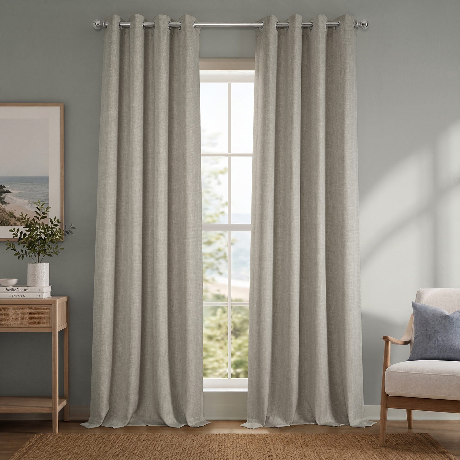 Pair of beige curtains hanging in a window with a view of greenery, a chair, and a side table with decor items.