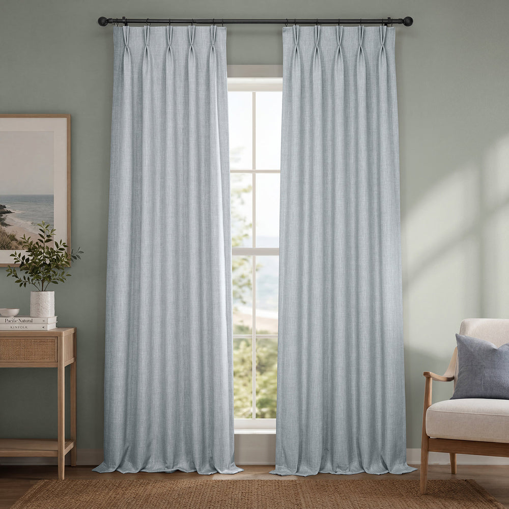 Light blue curtains hanging in a room with a window, chair, and side table.