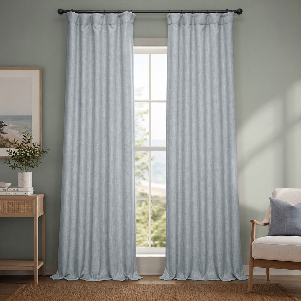 Light blue curtains hanging in a room with a window, chair, and side table.