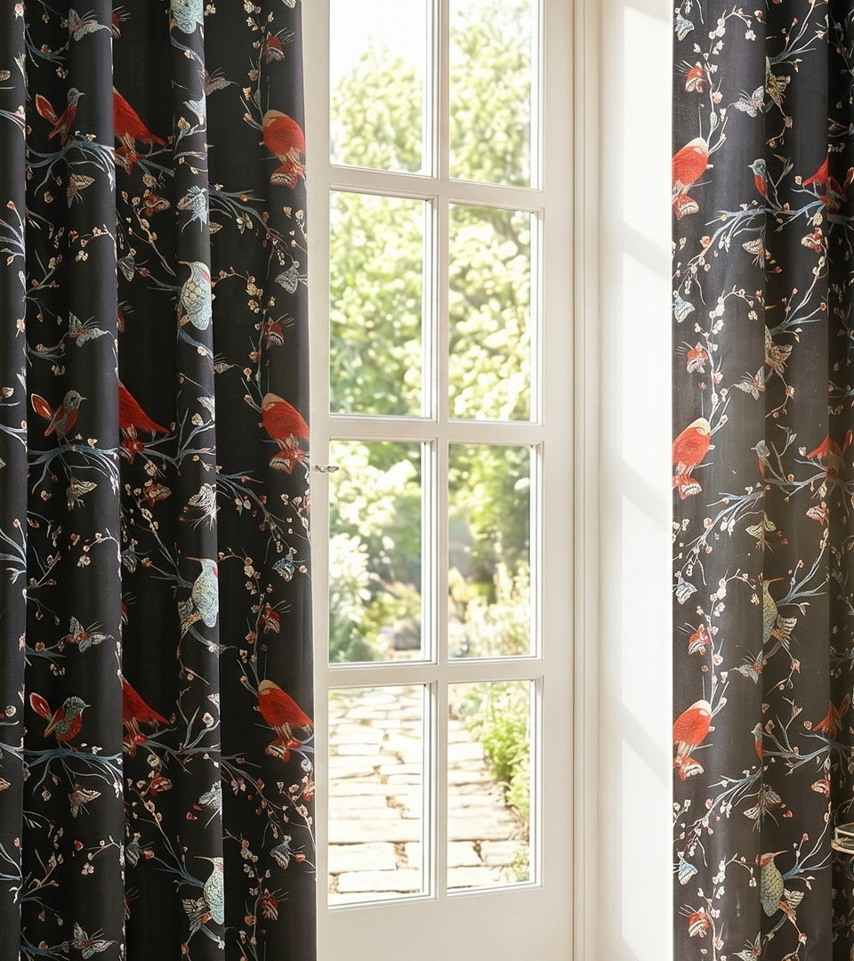 Designer black velvet curtains with colorful bird pattern hanging beside bright window.