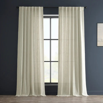 Beige curtains hanging in front of a window with a dark blue wall and light-colored floor.