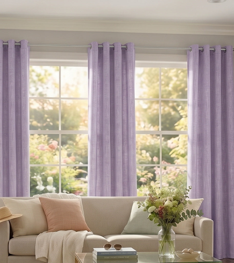 Lavender curtains framing large living room windows with a cream sofa, armchair, and soft natural light.