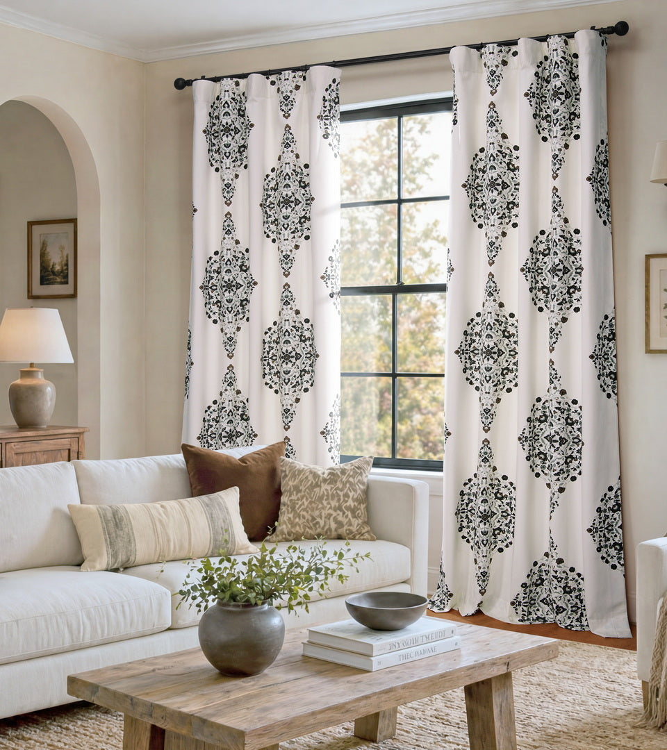 Ivory curtains with an intricate black and taupe medallion print bring timeless character and striking contrast to this inviting living room. The detailed pattern adds visual interest while blending beautifully with the warm wood accents, neutral furnishings, and layered textures for a sophisticated, welcoming space.