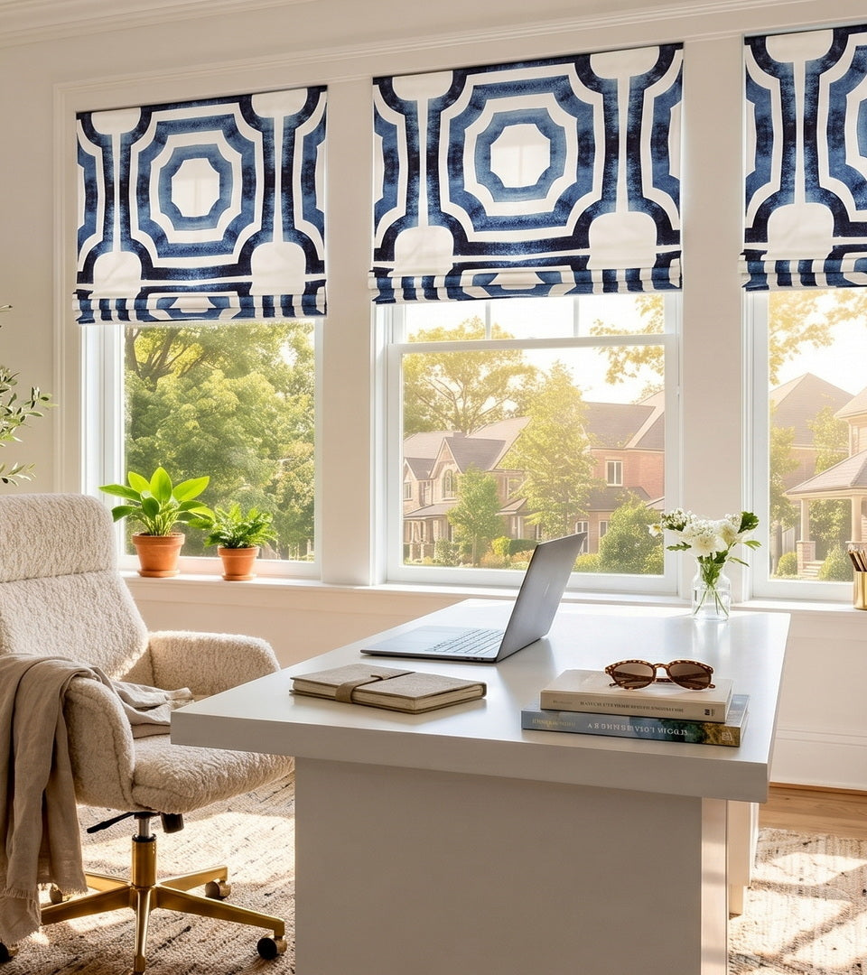 Mecca Blue patterned Roman shades covering home office windows above a white desk with potted plants and natural light.