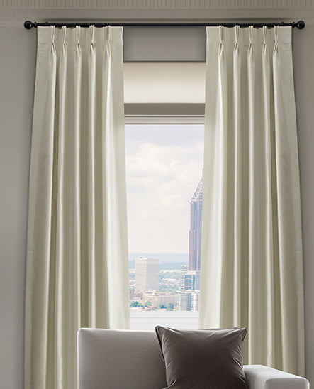 White pinch pleat curtains frame a tall window with a city view, creating an elegant, tailored look in a modern interior.