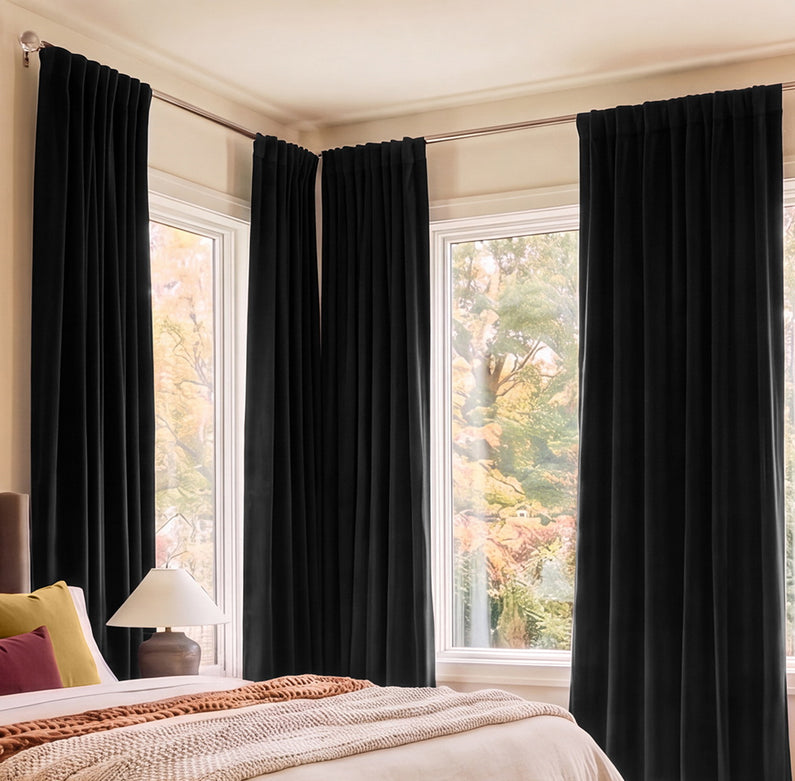 Black floor-length curtains frame tall bedroom windows, creating a bold contrast against warm neutral walls and an autumn view.