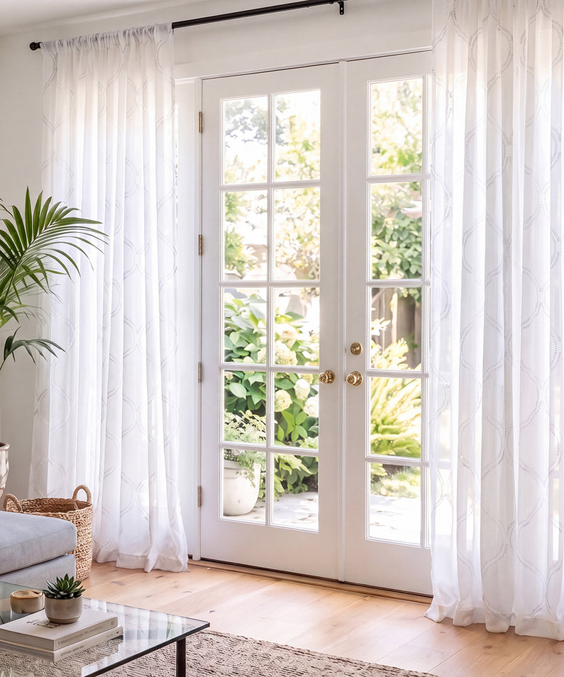 Sheer ivory patterned curtains softly filter sunlight in a cozy fall living room with warm autumn foliage and rust-toned accents.