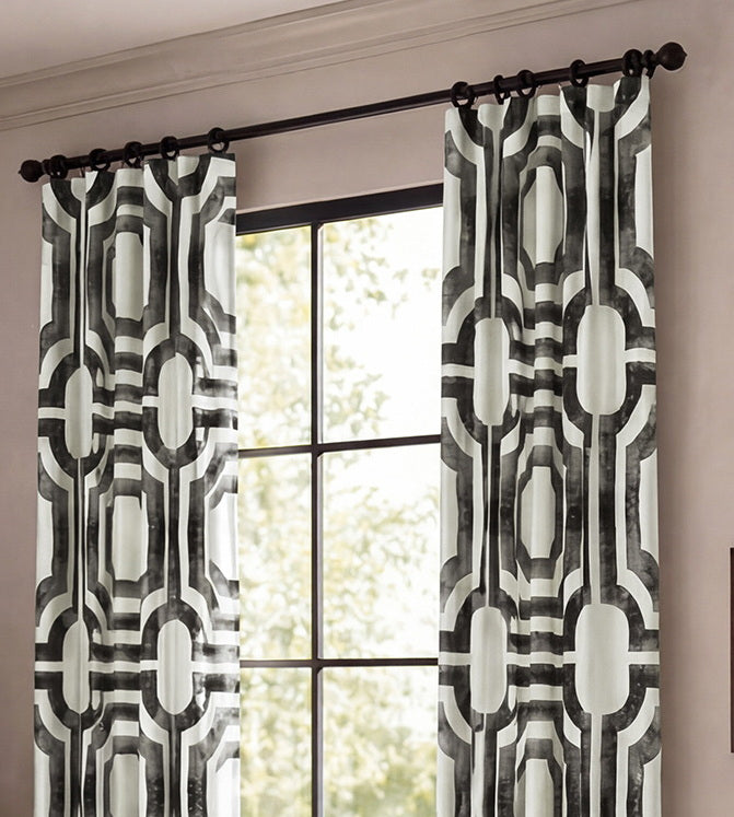 Black-and-white geometric patterned curtains hang from decorative rings, adding a modern statement to a bright, neutral living room.