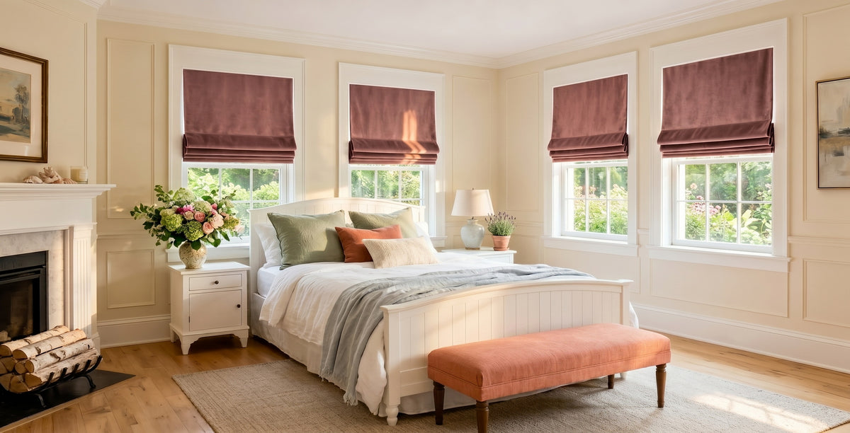 Wild Rose Heritage Plush Velvet Roman shades covering bedroom windows above a white bed with a fireplace and soft natural light.
